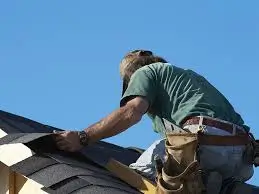 A skilled roofer laying shingles under a clear sky, showing expert workmanship by Roofing Whangarei.
